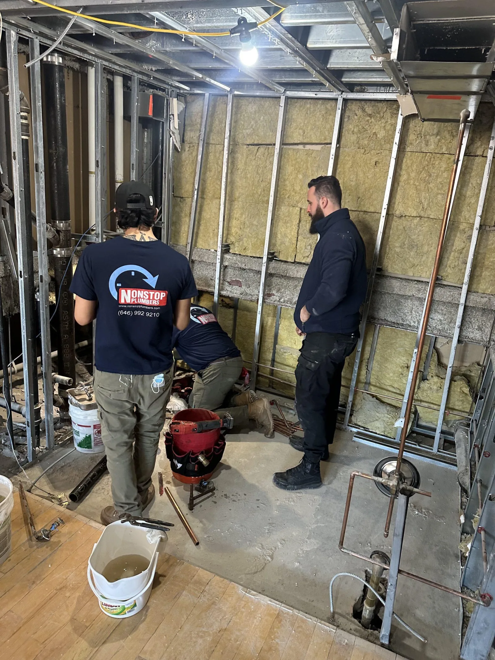 Nonstop Plumbers NY crew working on exposed plumbing inside a stripped-back room.