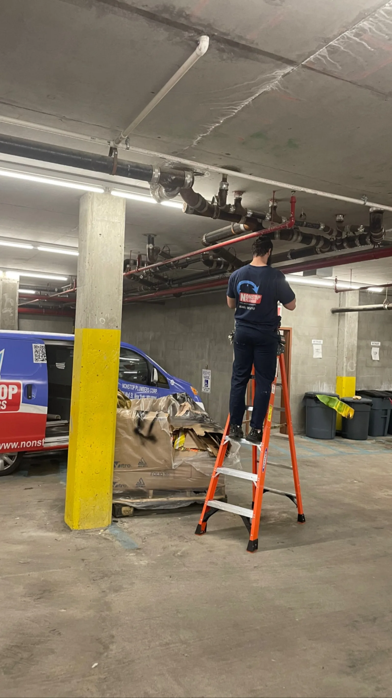 Nonstop Plumbers NY technician working beneath overhead fire suppression piping in a parking structure.